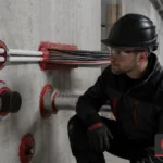 Technik kontrolujący zabezpieczenia przeciwpożarowe przejść kablowych i rurowych w ścianie